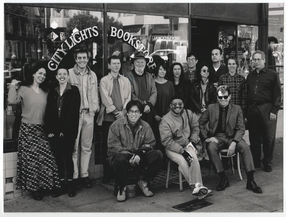 Group shot of 15 smiling City Lights staff members posing outside the storefront