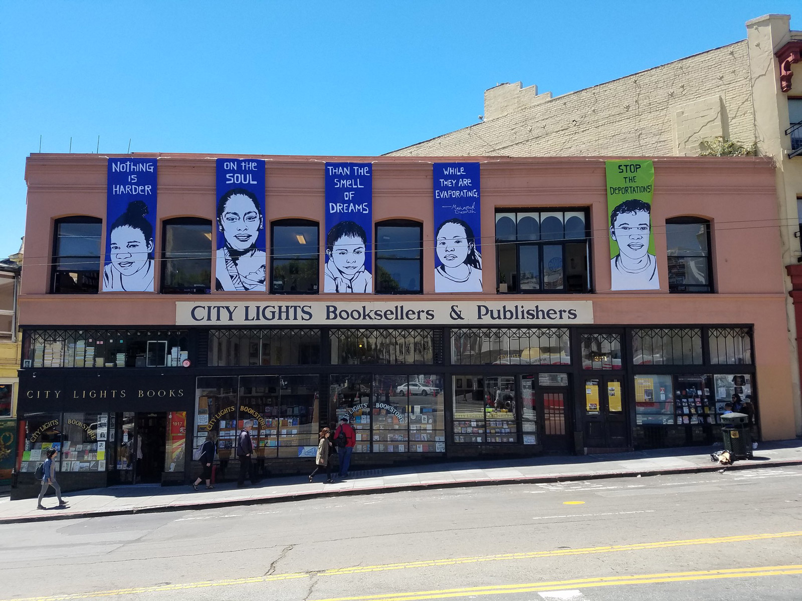 People walk by the City Lights storefront that is decorated with large blue banners