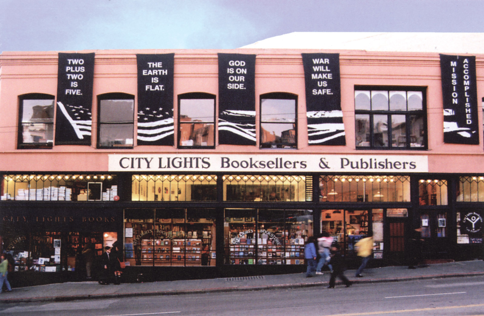 People walk by a lighted up City Lights storefront that is decorated with large black banners